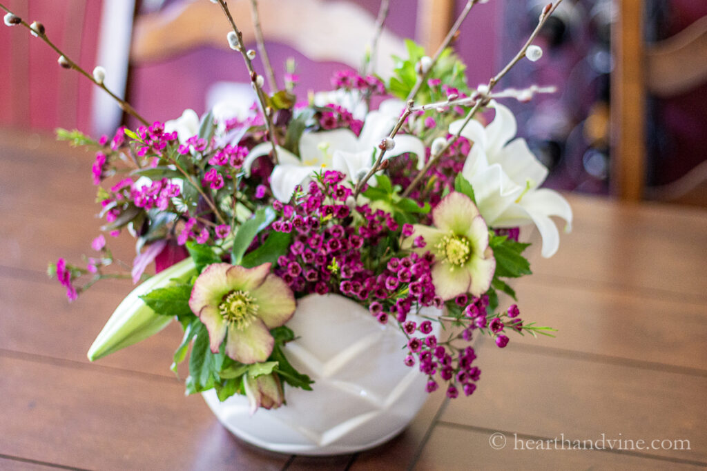 Flower arrangement in a white bowl with Easter lily flowers, pink wax flower and hellebores on an outdoor patio table.