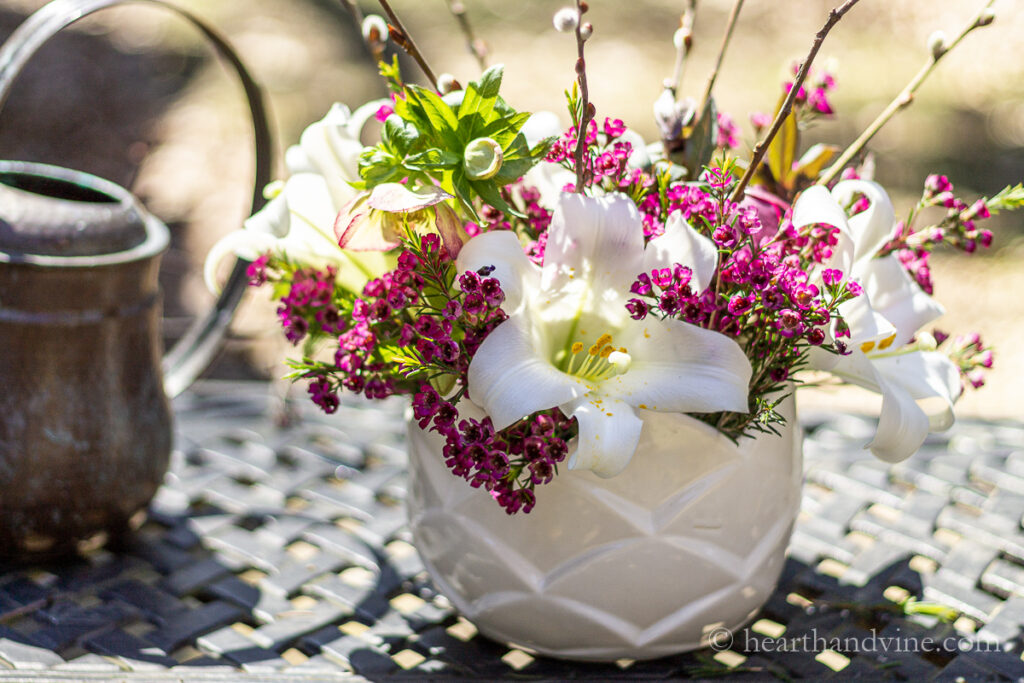 Flower arrangement in a white bowl with Easter lily flowers, pink wax flower and helebores on an outdoor patio table.