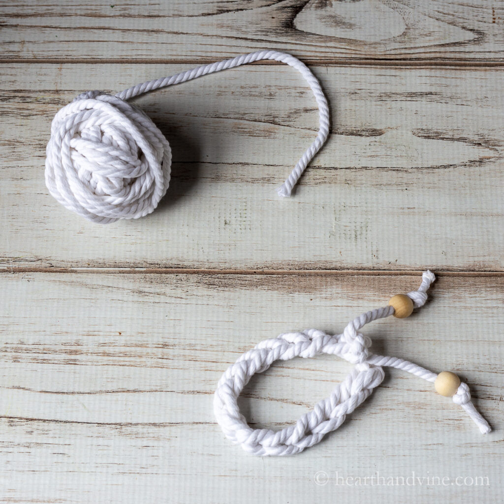 Ball of white craft cording next to a finger crocheted bracelet with wooden beads.