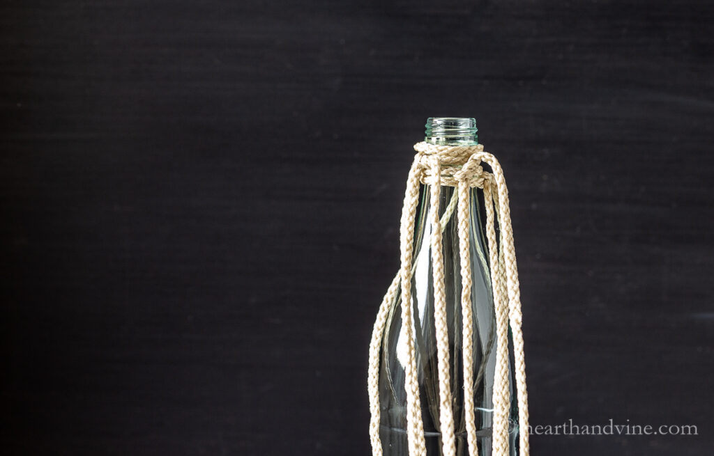 Four cords folded in half and tied to the neck of a tall glass water bottle.