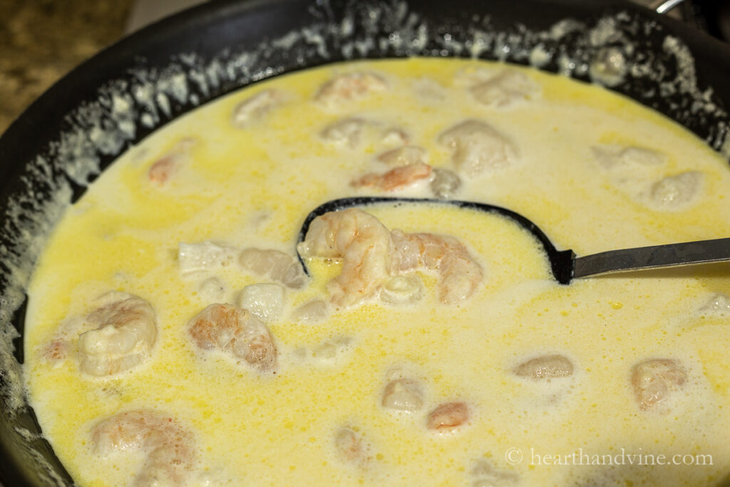 Large skillet with alfredo sauce, scallops and shrimp.