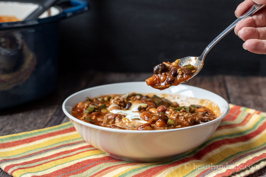 A spoon lifting a bit of ground turkey chili from a bowl.