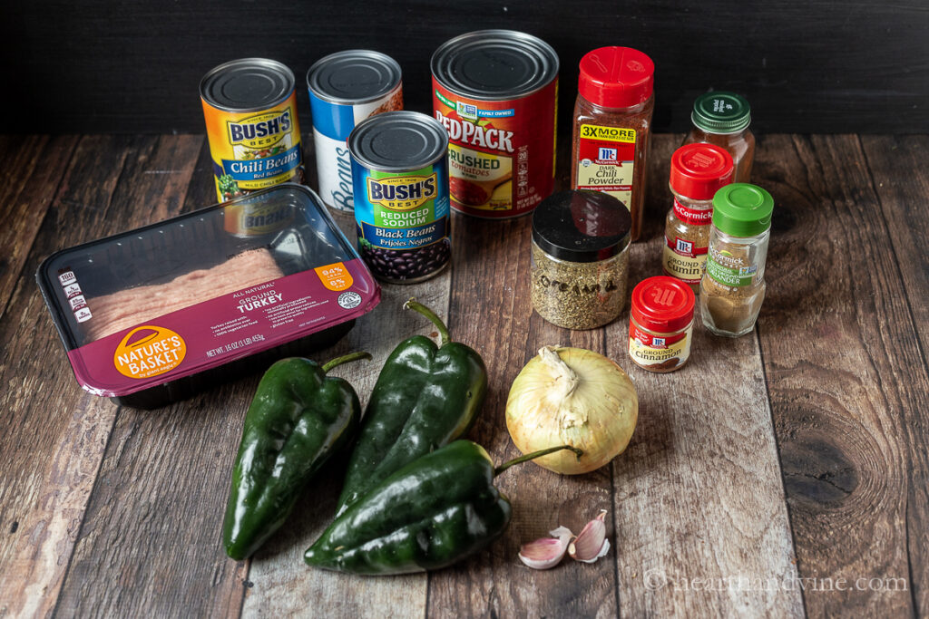Ingredients for ground turkey chili including poblano peppers, onion, garlic cloves, turkey, cans of beans and several spices.