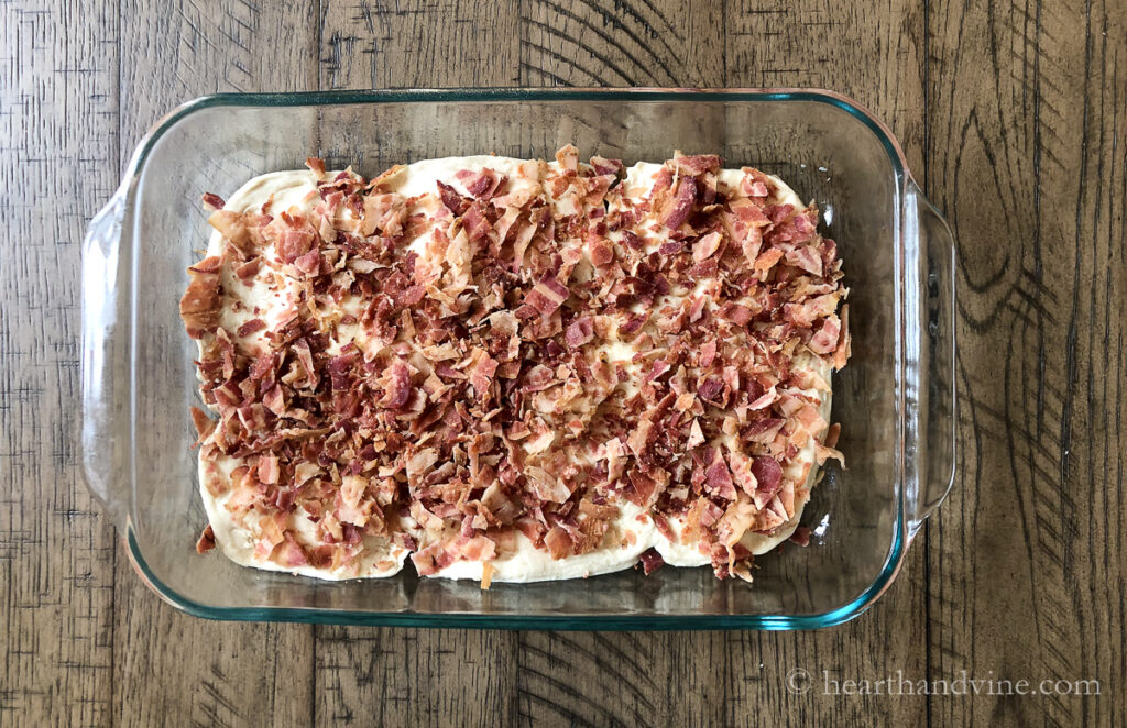 9 x 13 inch baking pan with a layer of biscuits followed by a layer of cooked bacon.