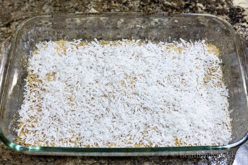 Butter, ground up graham crackers and shredded coconut layered in a 9 x 13 baking pan.