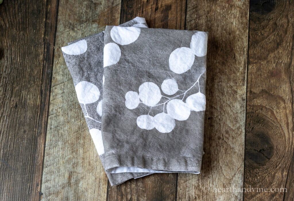 Two folded leaf printed napkins in gray and white on a table.