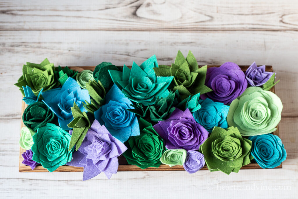 Felt succulents shapes in shades of green, blue and purple in a wooden planter.