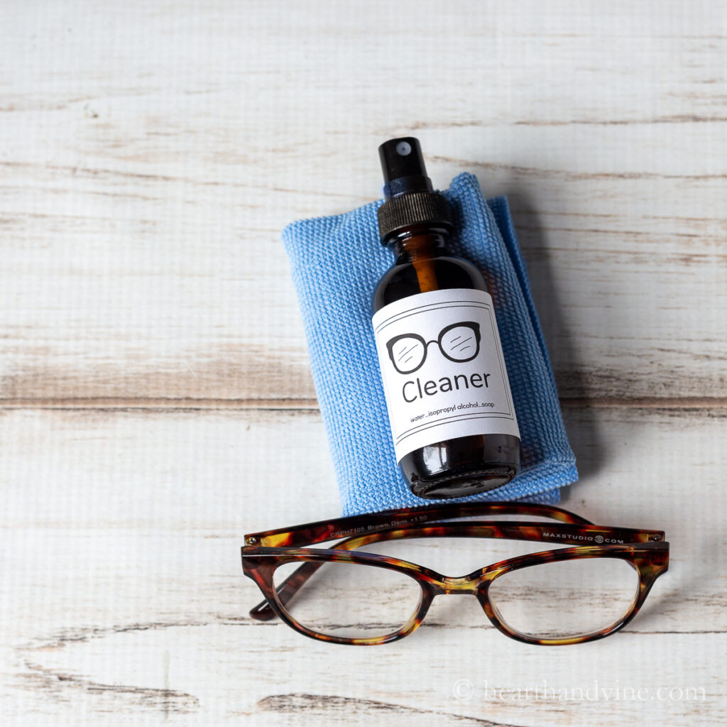 Small bottle of eyeglass cleaner on a microfiber towel and a pair of glass next to it.