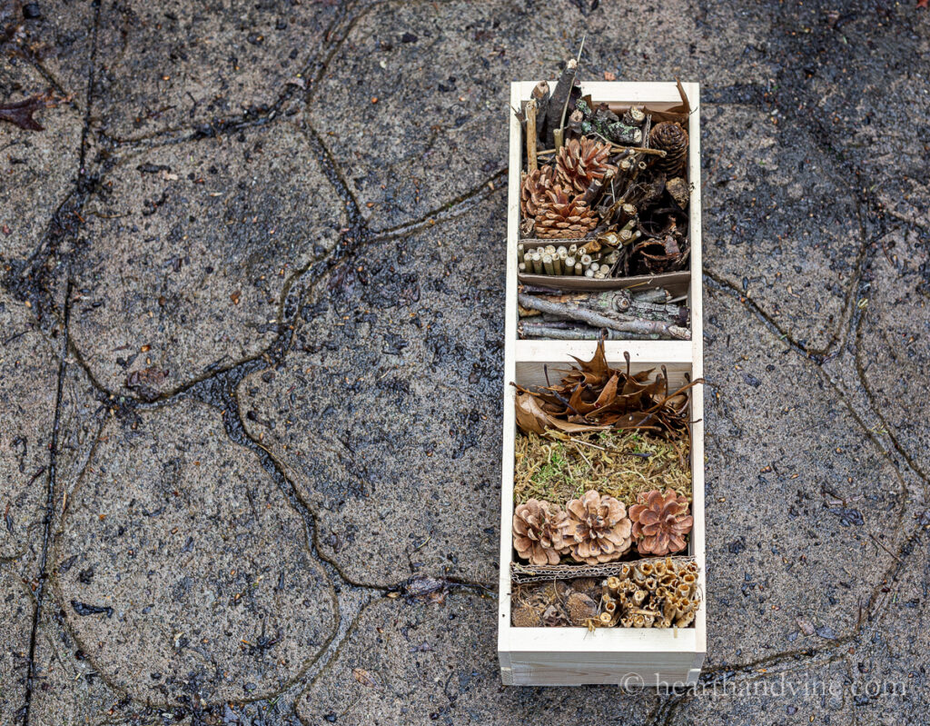 Completed bug house with sticks, bark, reeds, bamboo, pine cones and moss on a patio.