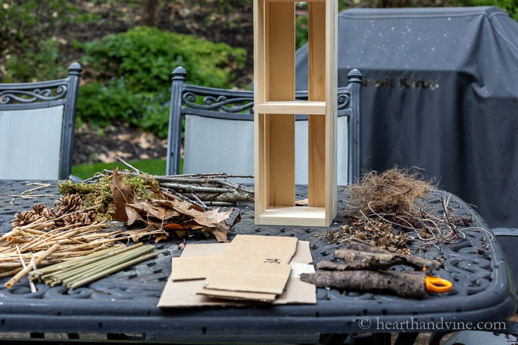 A tall wood crate, dried leaves, bark, cardboard, reeds, bamboo and moss on a table.