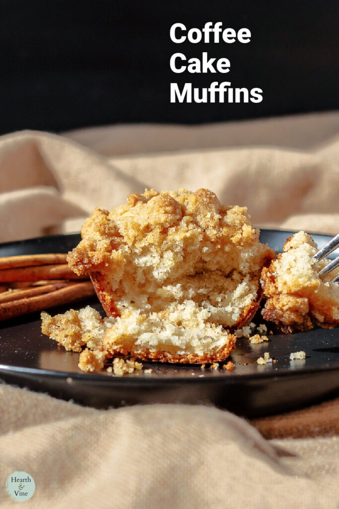 A coffee cake muffin broken open with a fork with cinnamon sticks on the side.