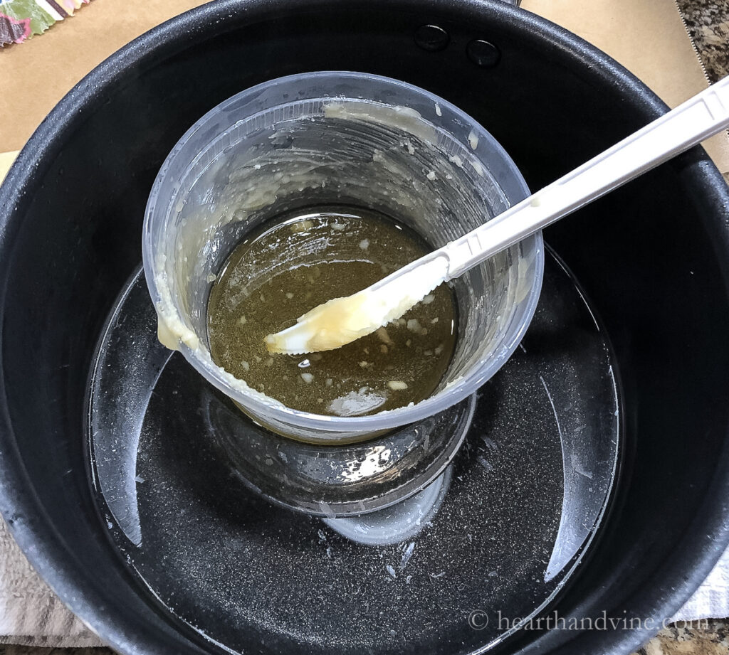 Small plastic container in an old pot with a little water. The container has some beeswax mixture that is melting.