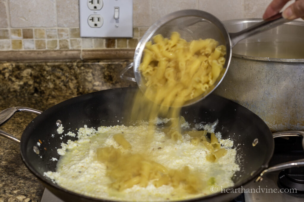 A basket lifting pasta out of boiling water directly into a pan with lemon ricotta sauce.