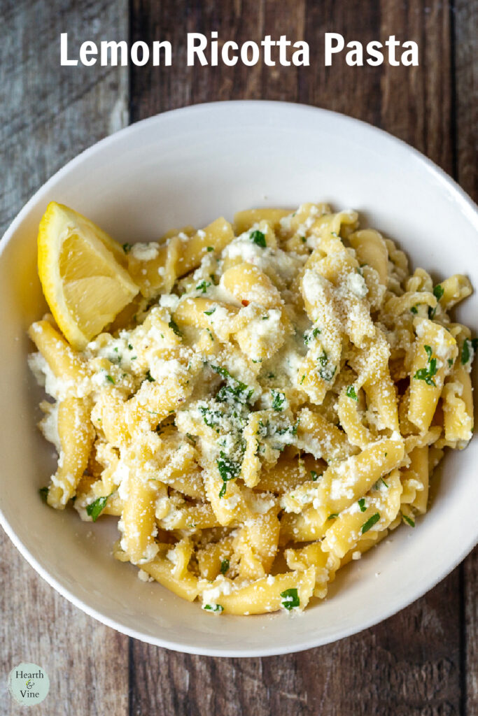 Bowl of lemon ricotta pasta with a wedge of lemon and extra Parmesan cheese.