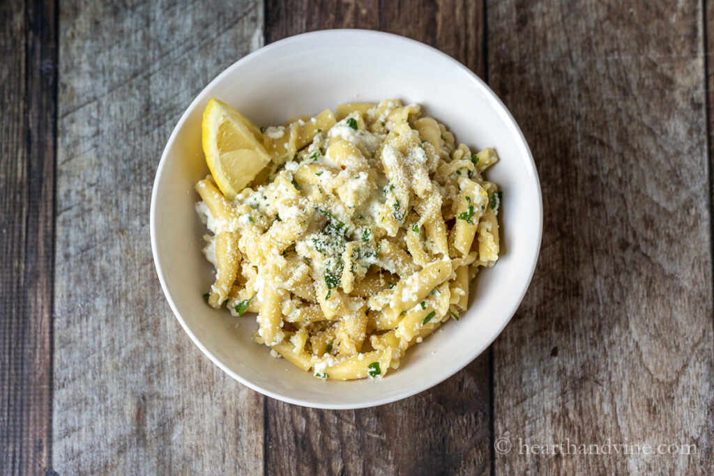 Small white bowl with lemon ricotta pasta, extra Parmesan and a lemon wedge.