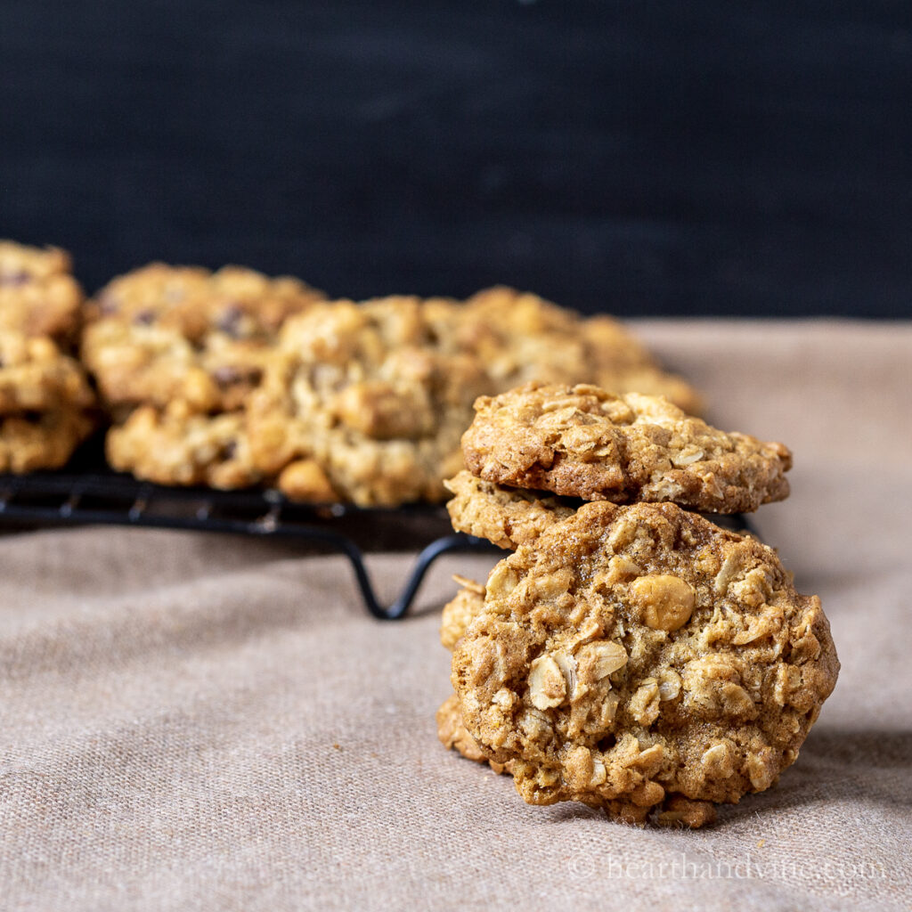 One facing oatmeal butterscotch cookie in front of a stack of cookies and a rack of more cookies.