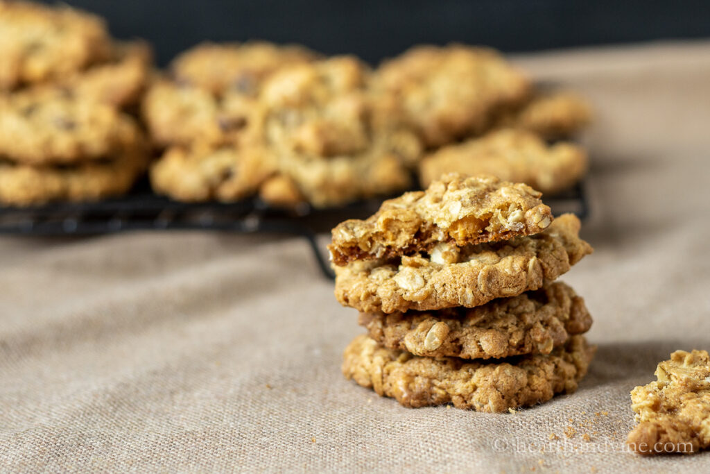 Stack of oatmeal scotchies cookies in front of a rack filled with cookies.