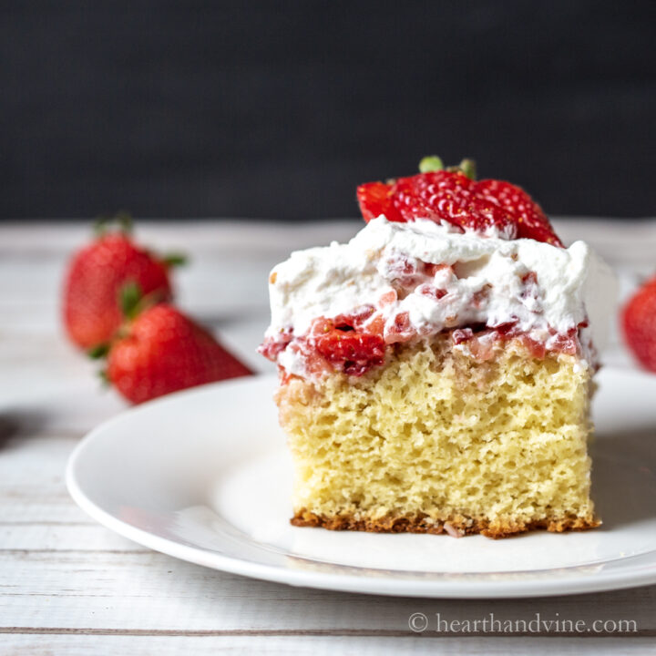 Serving of strawberries and cream cake with fresh strawberries on top and on the table.