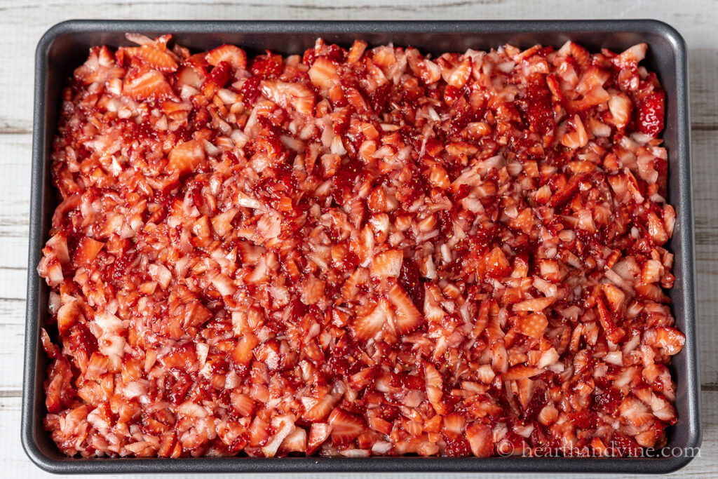 Chopped up strawberries on top of a sheet pan cake.