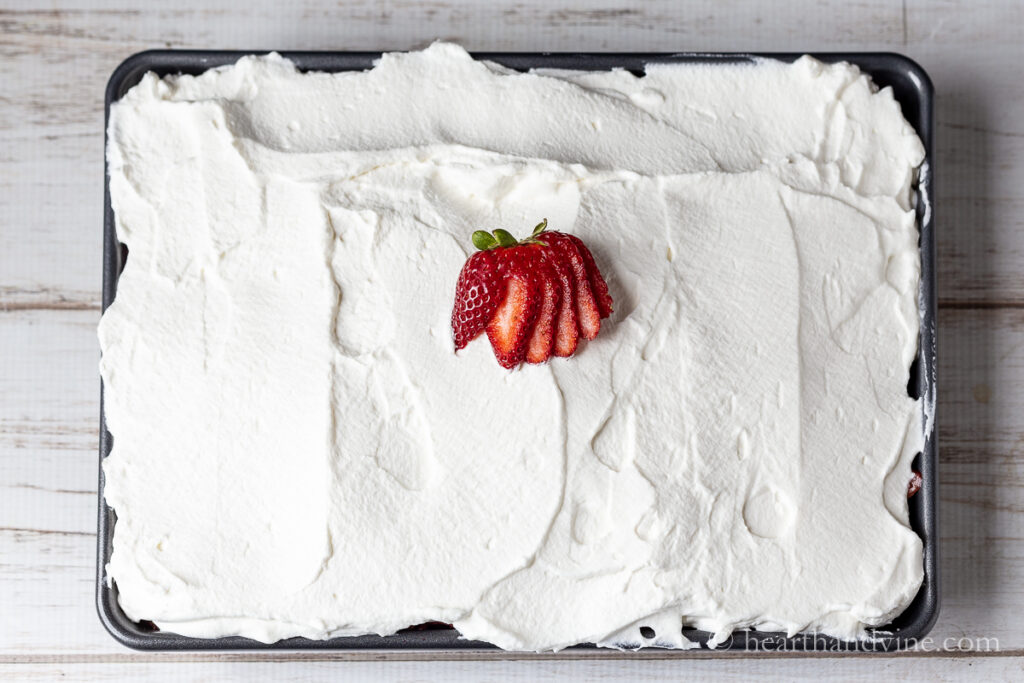 Cake with strawberries and cream in a sheet pan with a strawberry garnish.