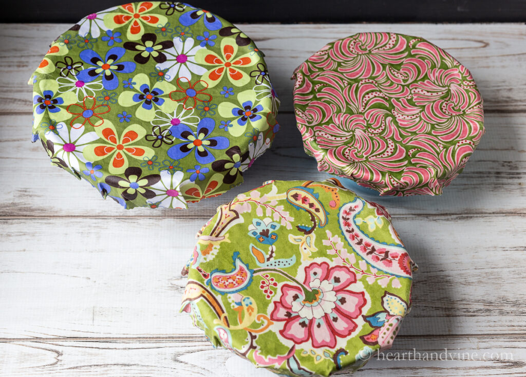 Three diy beeswax wraps on ceramic bowls in brightly colored prints.