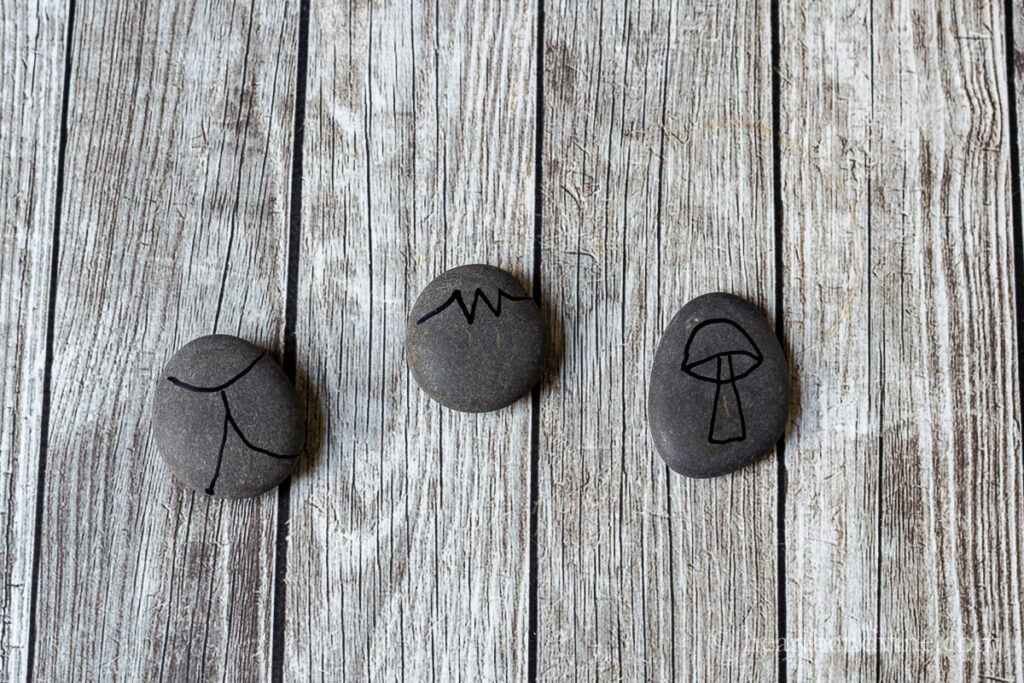 Three rocks with black outlines. One is a ladybug, one a strawberry and one is a toadstool.