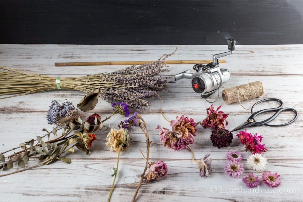 Dried flowers, a fish reel, twine, scissors and a dowel rod.