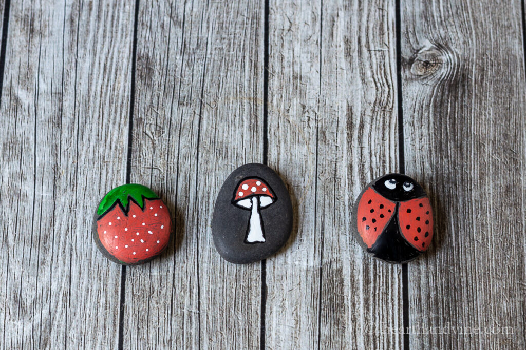 Three color painted rocks. One is a strawberry, one a toadstool and one is a  ladybug.