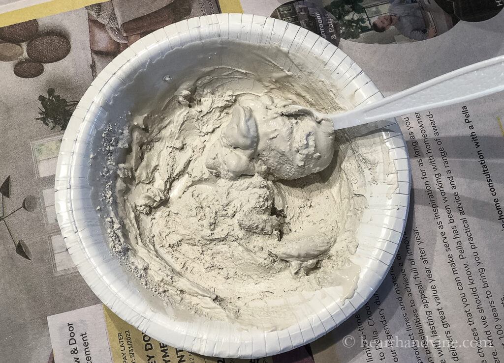 Thick mixture of Plaster of Paris and water in a paper bowl with a plastic spoon.