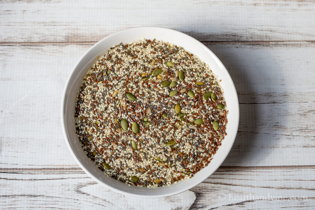 A white bowl with water, sunflower, pumpkin, flax, chia and sesame seeds.