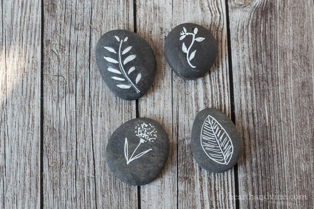 Four botanical painted rocks with white paint only.