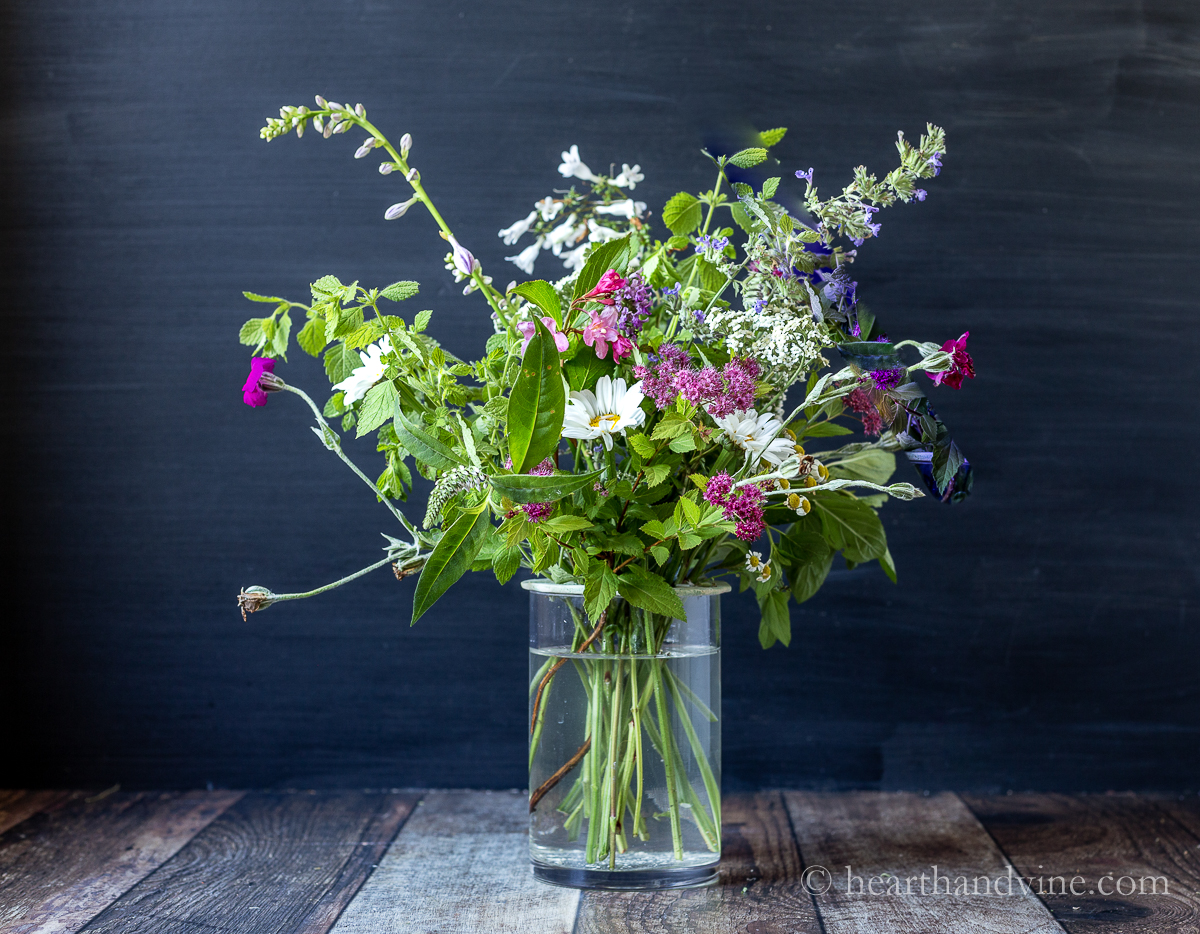 Large ground of various garden flower in a cylindrical vase using a clay flower frog.