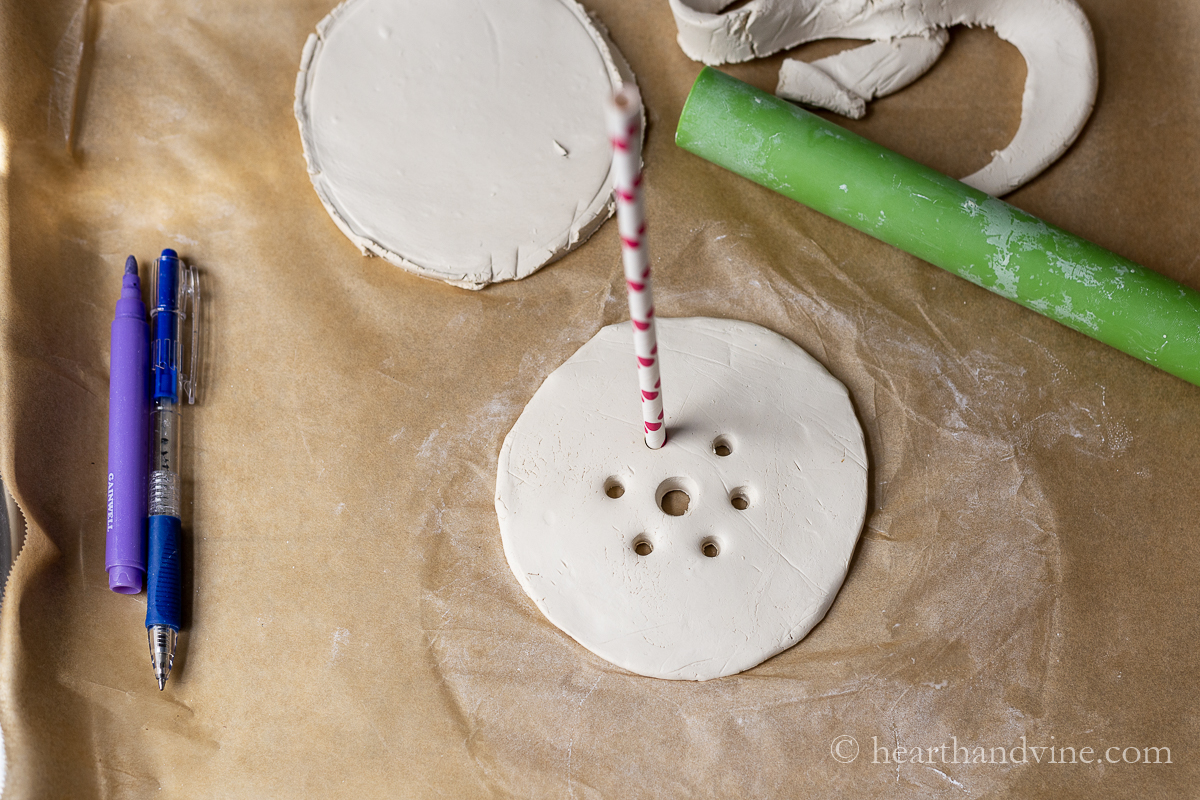 A straw making small holes around a center hole in a clay disc.