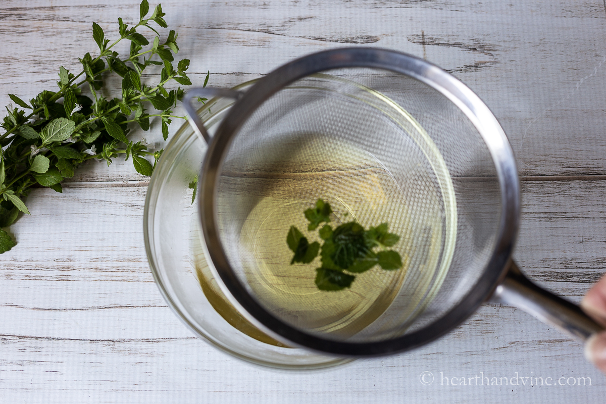 Strainer over a bowl straining out lemon balm leaves from tea.