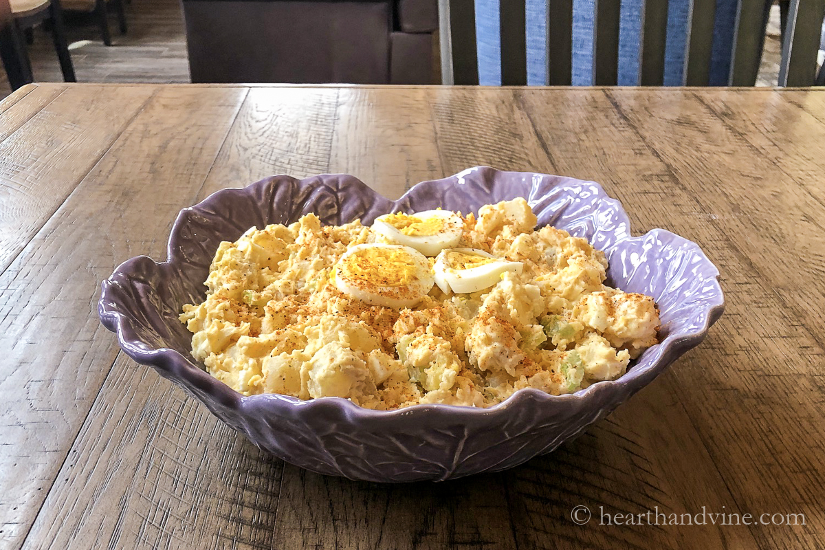 Ornate cabbage serving bowl filled with old fashioned potato salad topped with sliced boiled eggs.