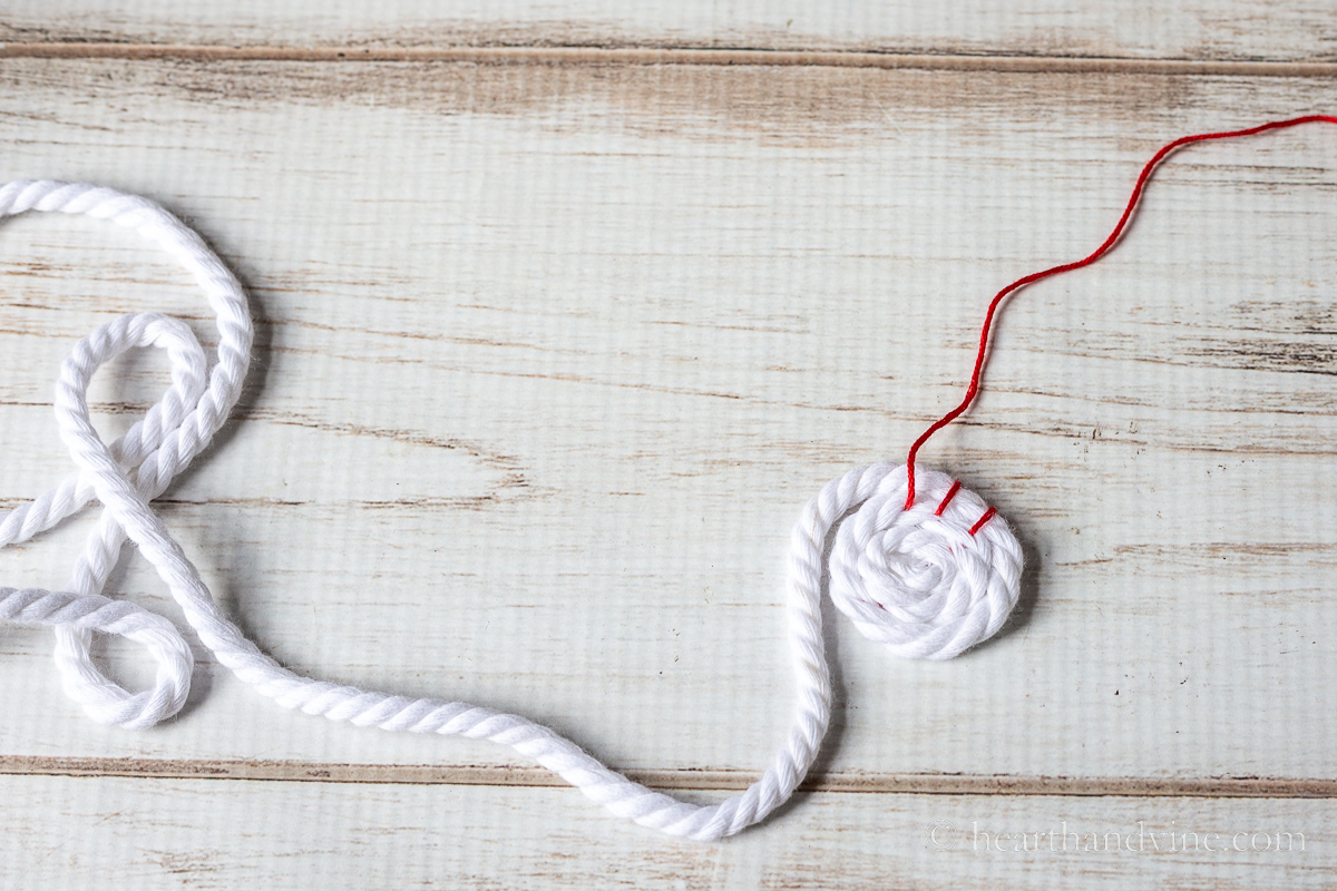 Tiny coil of white rope with a few red embroidery floss stitches.