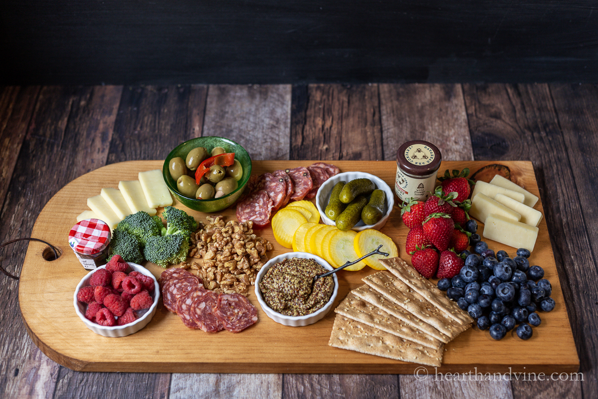 Large wooden charcuterie board filled with cheeses, crackers, fruit and more.