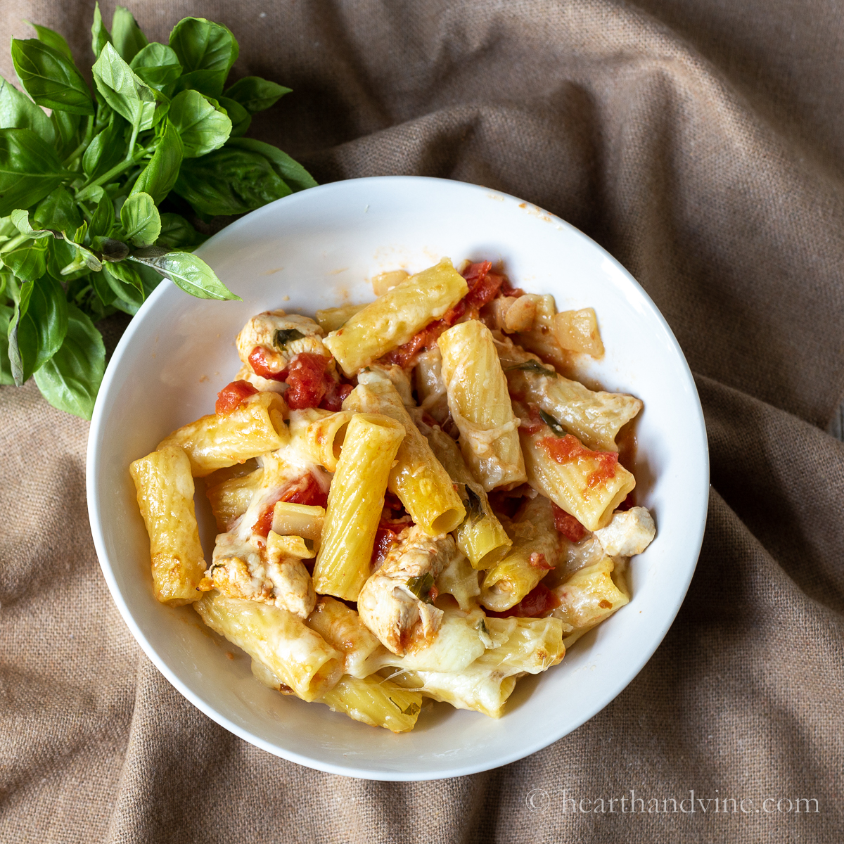 Individual serving bowl of chicken pasta bake next to some fresh basil.