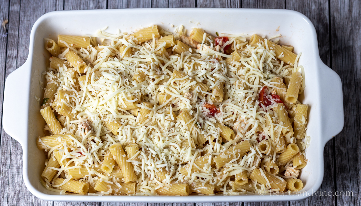 Chicken pasta bake noodles and sauce and shredded cheese in a large 9 x 13 baking pan before baking.