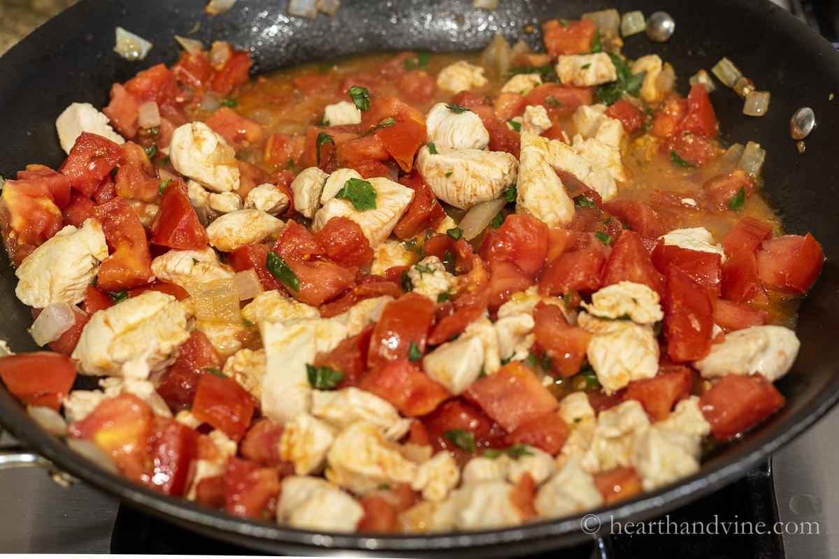 Large skillet with chicken, onions, tomatoes, and basil.