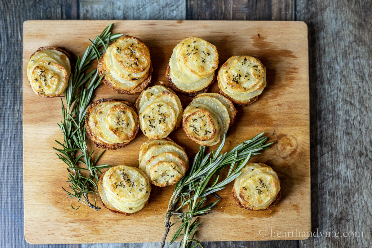 Stacks of thin potato slices with baked until golden on a wood board with sprigs of fresh rosemary.