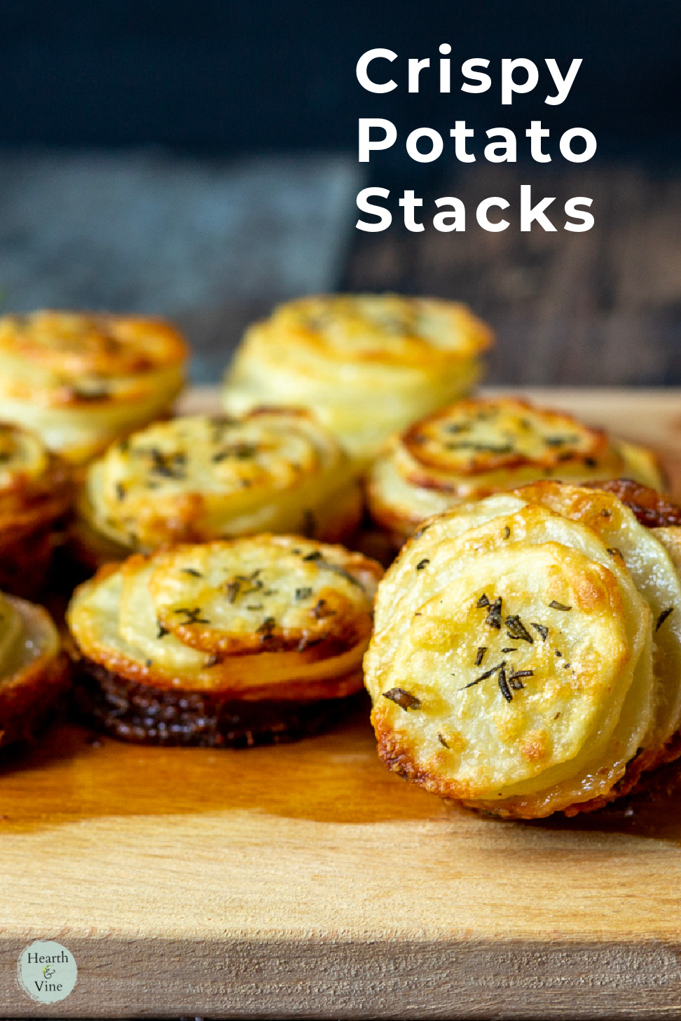 Crispy potato stacks with Parmesan and chopped rosemary leaves on a board.