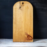 Rounded wooden board with hole at one end and a leather hanger.