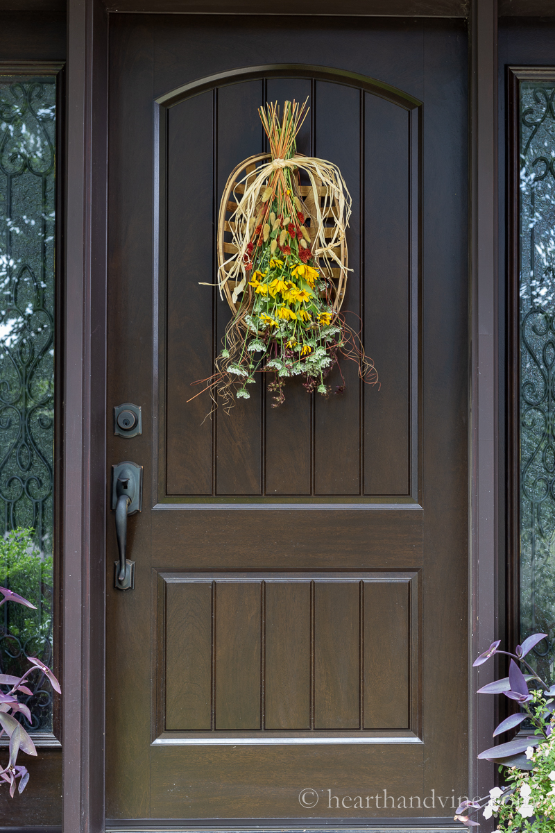 Fall flower swag on a tobacco basket hanging on a brown front door.