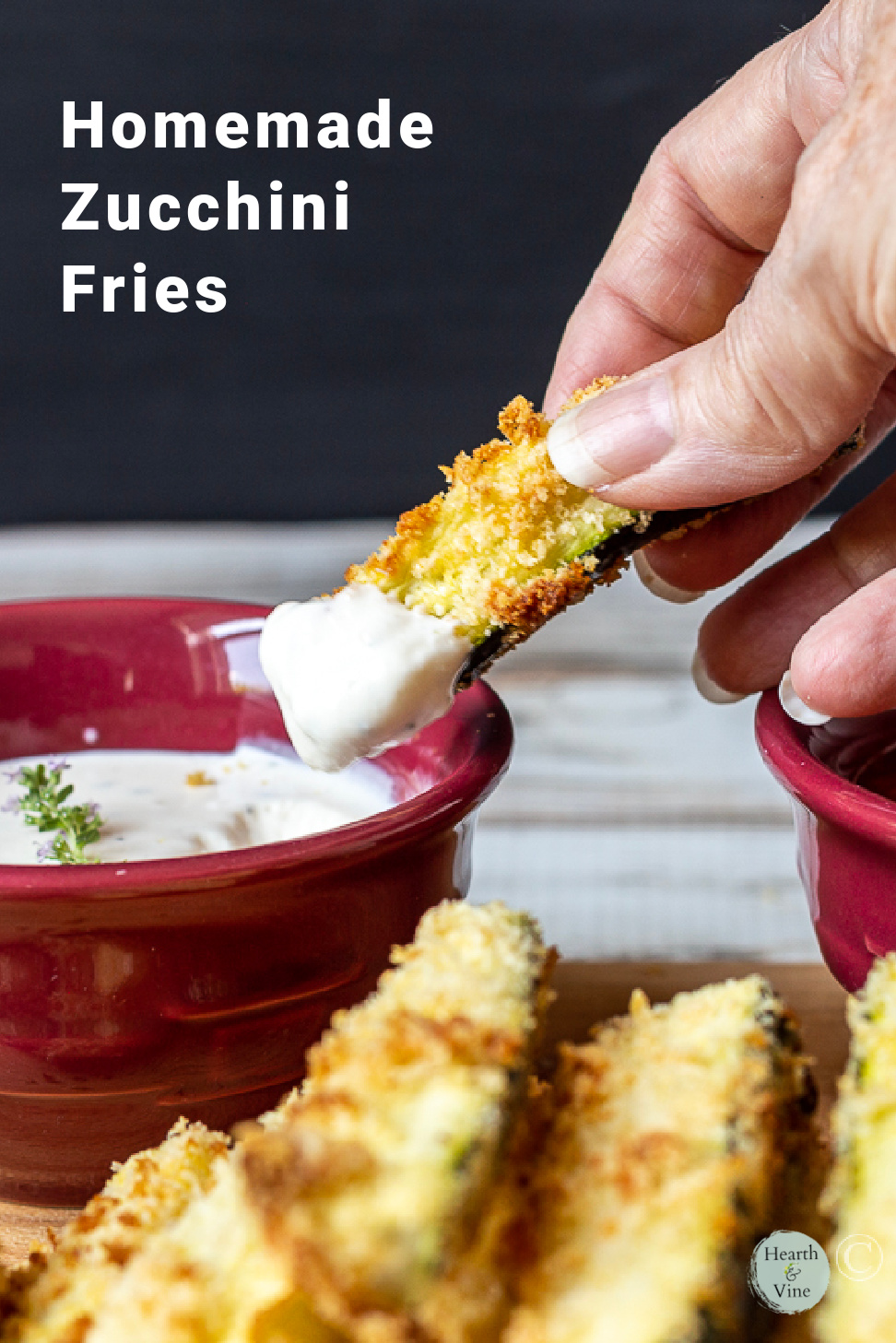 A hand dipping a baked zucchini fry in ranch dressing.