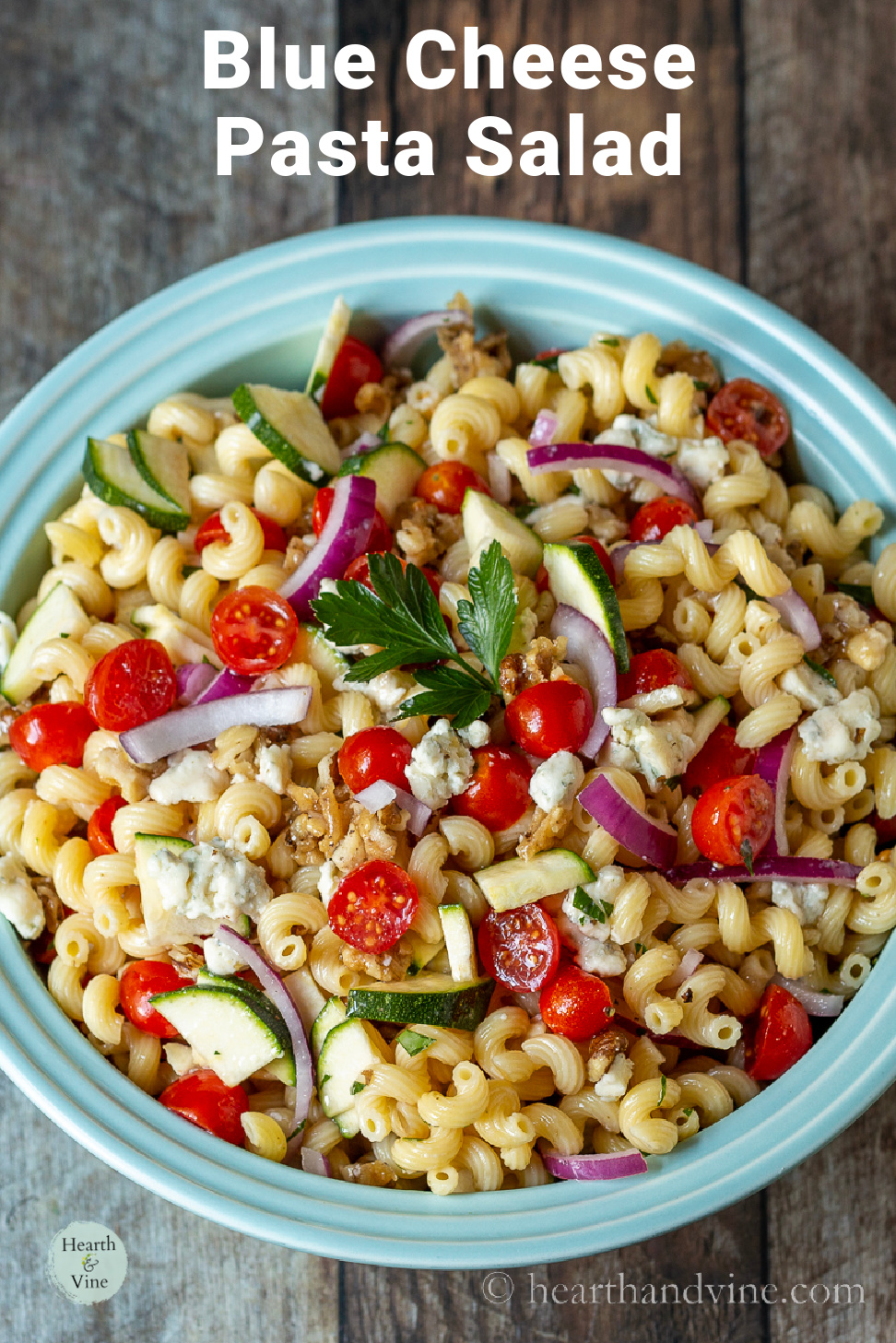 Overhead view of blue cheese pasta salad with candied walnuts, red onion, zucchini, tomatoes, and parsley.