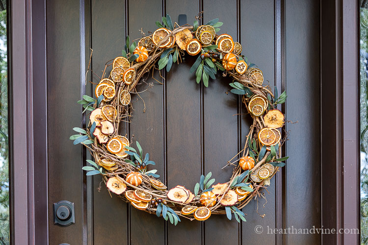 Grapevine wreath with dried orange slices, dried oranges, dried apple slices and a few sprigs of faux greenery.