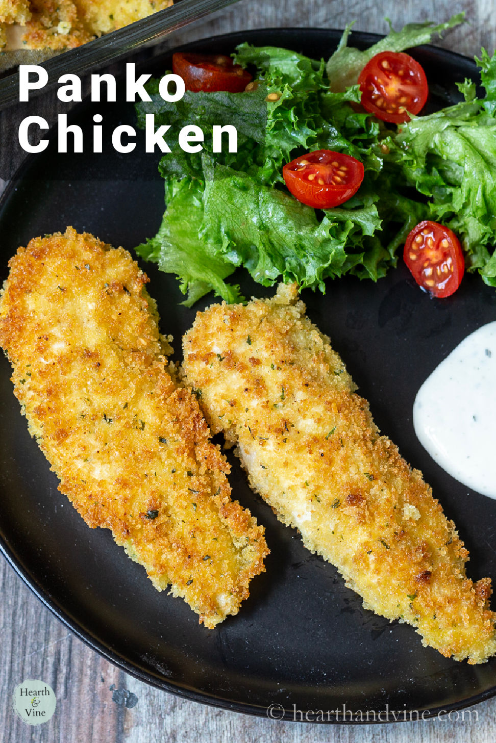 Black plate with 2 panko chicken strips, ranch and a small salad.