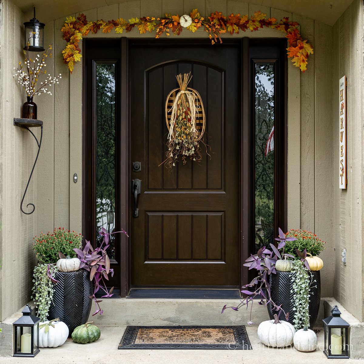 Front door fall decor with mums, pumpkins and a leaf garland