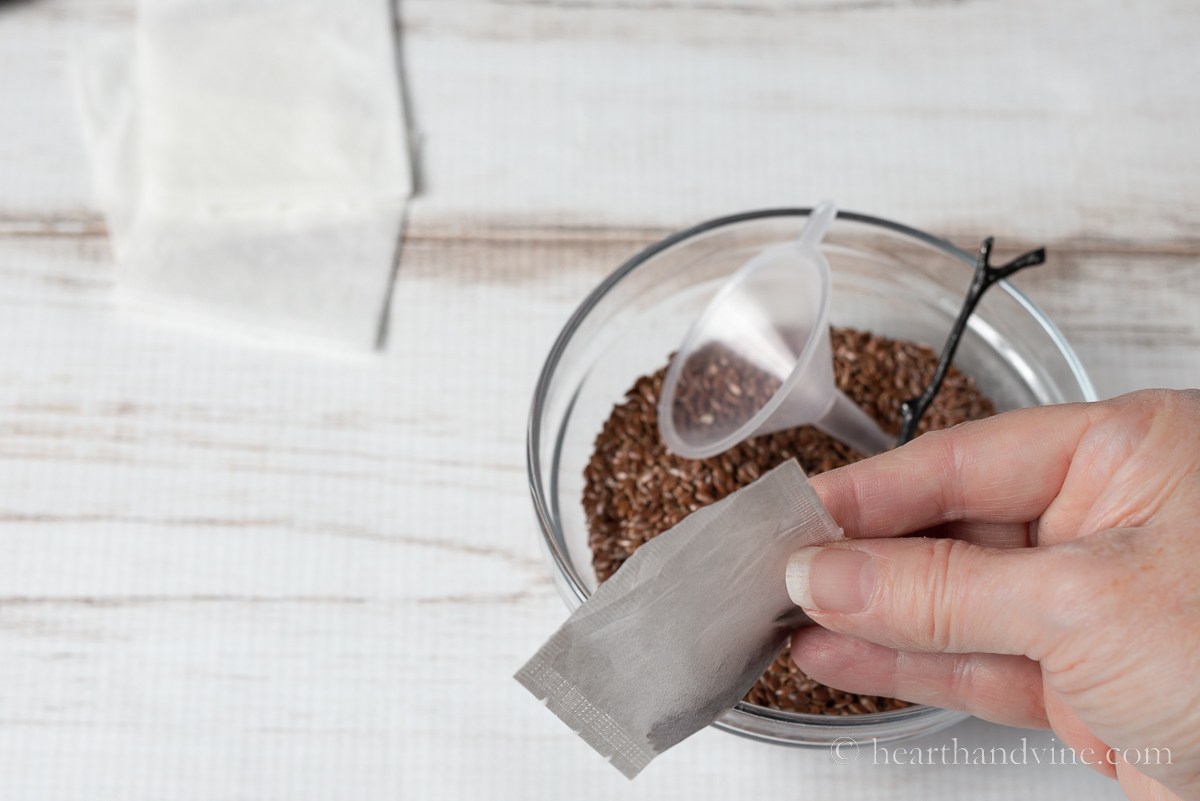 A hand holding a fillable teabag over a bowl of flaxseed.